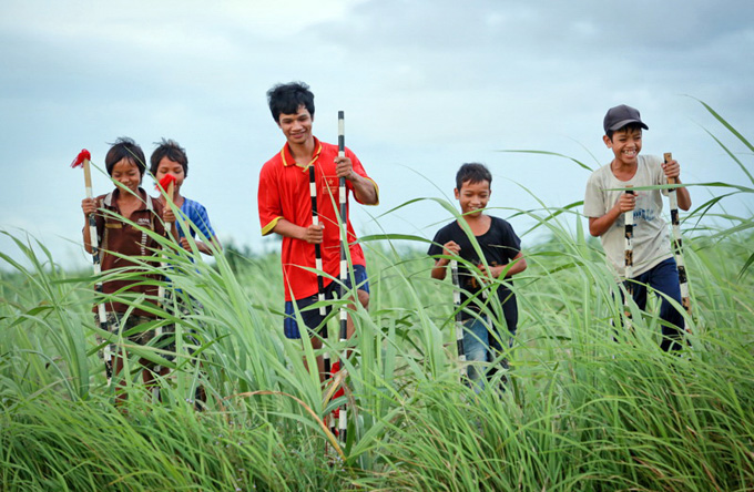 Dinh Blin, 23, dressed in a red T-shirt, teaches boys how to move on stilts on a sugar cane field.