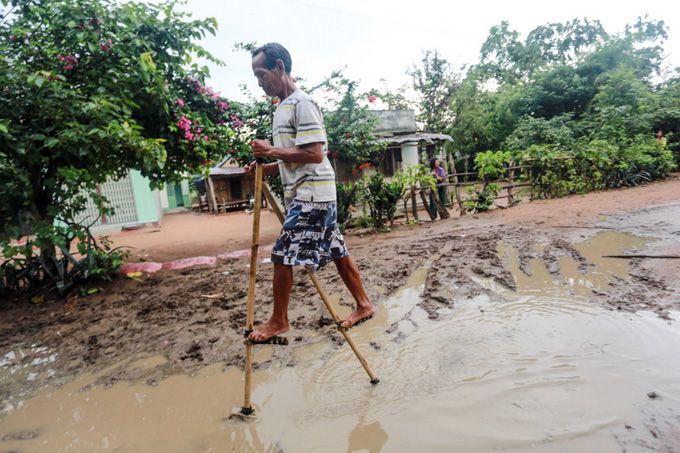 Dinh Bol, 48, gets across a muddy road using stilts.