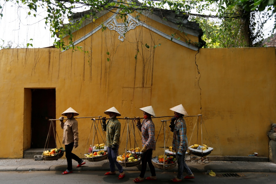 Women wearing traditional hats, known as non la, sell fruits in Hoi An, Vietnam April 4, 2016.