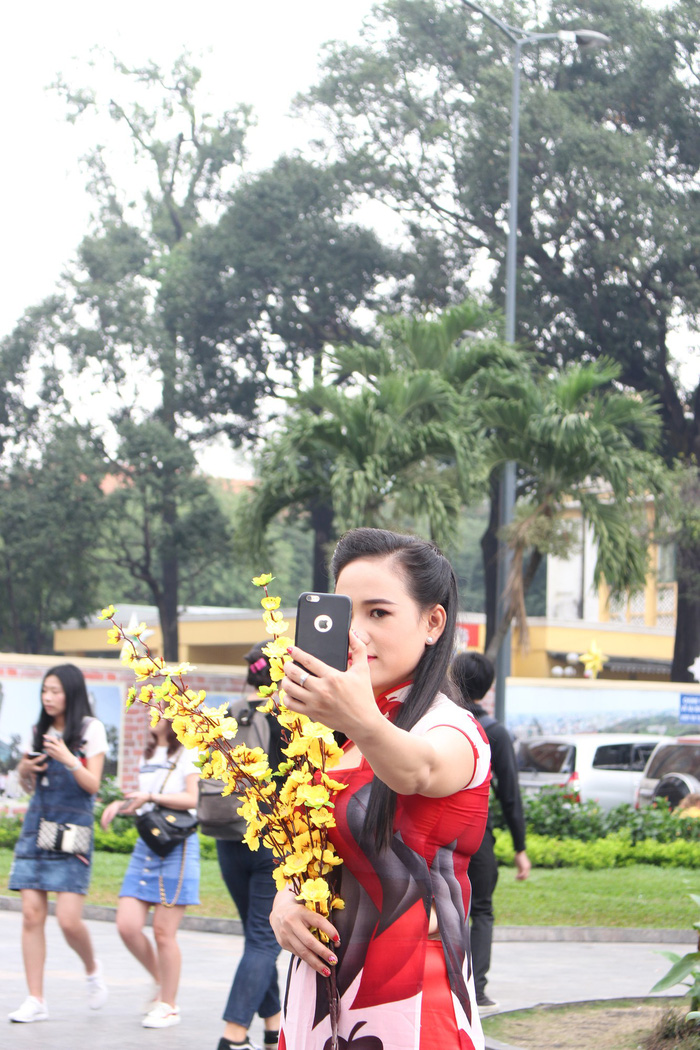 A woman in the short-sleeved transformed ao dai takes selfies with false yellow apricot flowers. Photo: Tuoi Tre