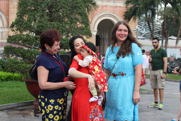 Foreign visitors take a picture with a Vietnamese mom and her baby in red outside the Notre-Dame Cathedral Basilica of Saigon. Photo: Tuoi Tre