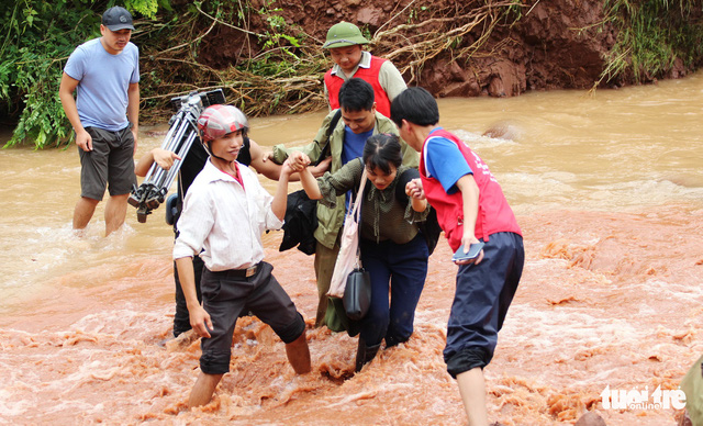 Reporters and members of the Red Cross in Lai Chau cross a stream to help locals in Noong Heo Commune.