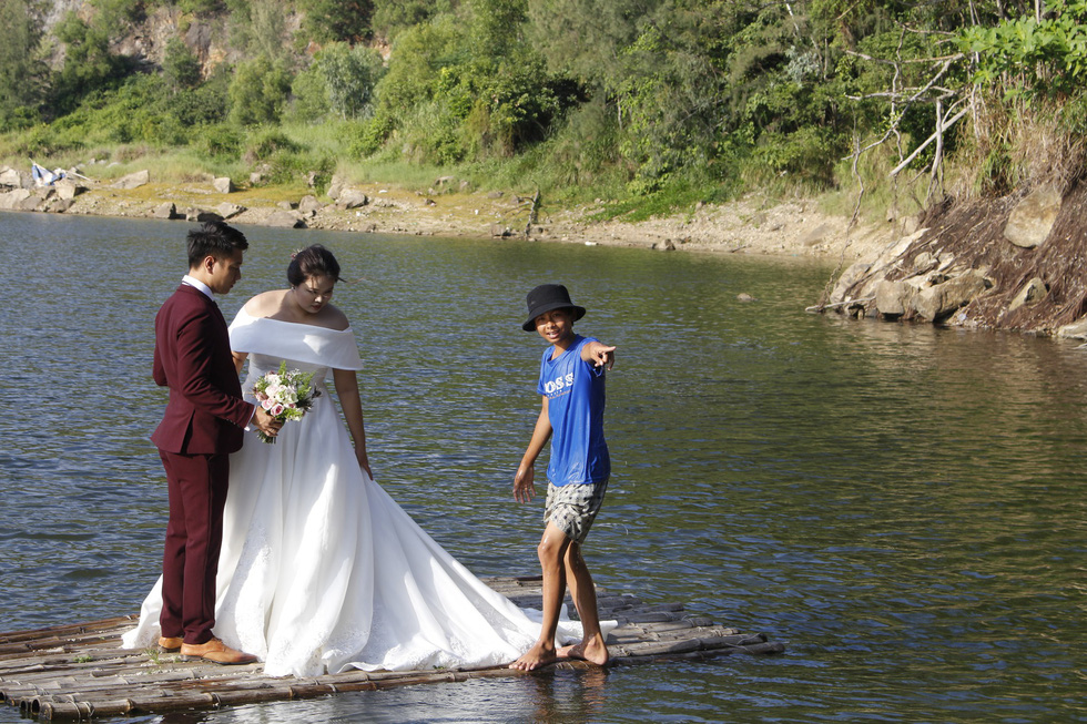 Tai, a teen boy who controls bamboo rafts to carry couples for photo shoots at the Green Lake in Da Nang, shows a couple how to pose for their wedding photo. Photo: Tuoi Tre