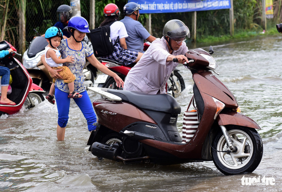 A man pushes his broken down motorcycle on a flooded road.