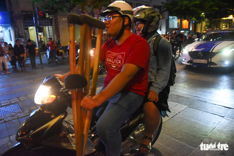 A couple carrying a pair of crutches joins the crowd of people on motorbikes touring around the Nguyen Hue pedestrian area on November 16, 2018. Photo: Tuoi Tre