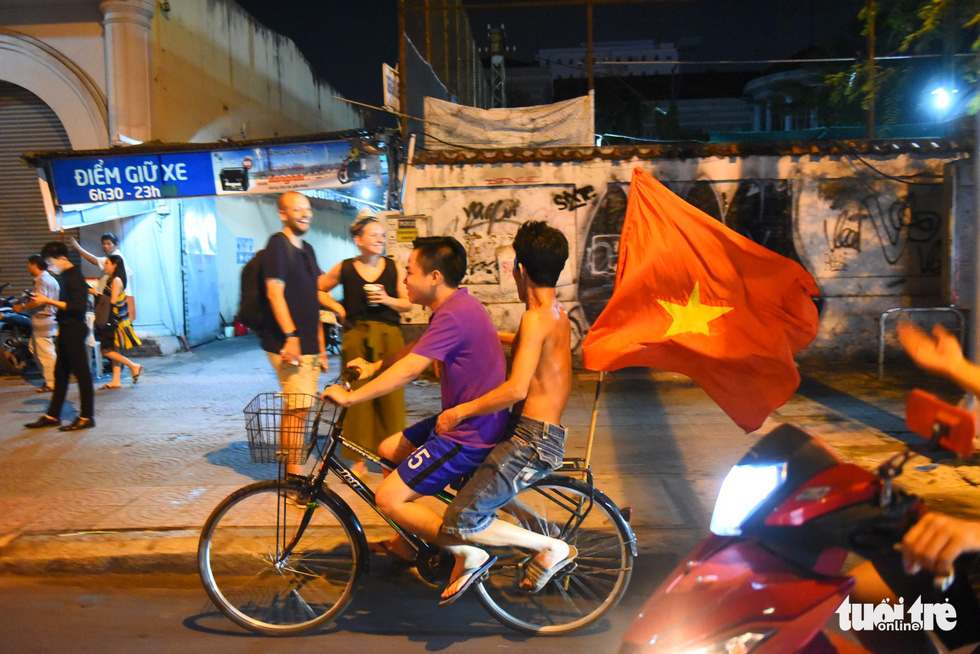 Two young men ride a bicycle that carries a Vietnam national flag at the end to celebrate Vietnam's 2-0 victory against Malaysia at the 2018 AFF Championship on November 16, 2018. Photo: Tuoi Tre