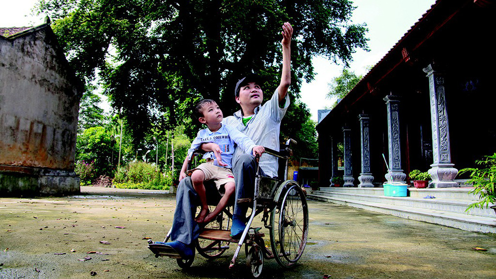 Phung Van Truong sits in a wheelchair with his son in a village in suburban Hanoi, Vietnam. Photo: Tuoi Tre