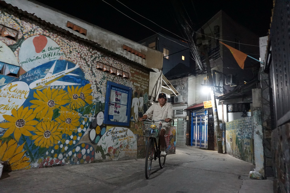 Nguyen Van Minh rides his bicycle in front of an alley wall he painted in Ho Chi Minh City, Vietnam. Photo: Tuoi Tre