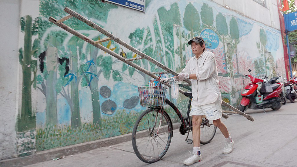 Nguyen Van Minh walks his bicycle in front of an alley wall he painted in Ho Chi Minh City, Vietnam. Photo: Tuoi Tre