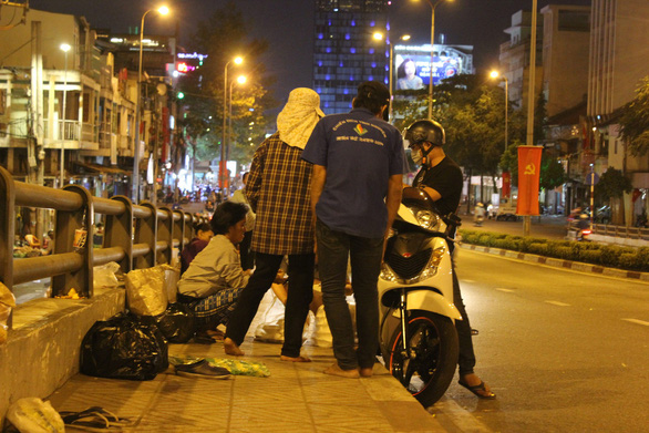 As a generous man stops his motorbike to distribute gifts to beggars for lunar new year, many beggars quickly gather. Photo: My Lang / Tuoi Tre