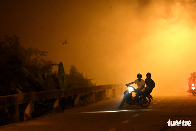 Two motorbike riders make a U-turn on a smoke blanketed road near a grassland fire in Dong Nai Province, southern Vietnam, March 3, 2019. Photo: A. Loc / Tuoi Tre
