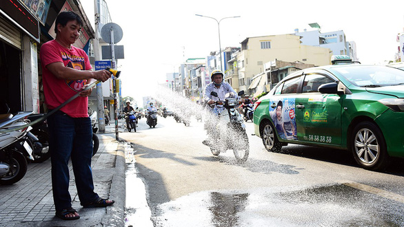 A man sprays water at the street in front of his house to cool down the heat in Phu Nhuan District. Photo: Duyen Phan / Tuoi Tre