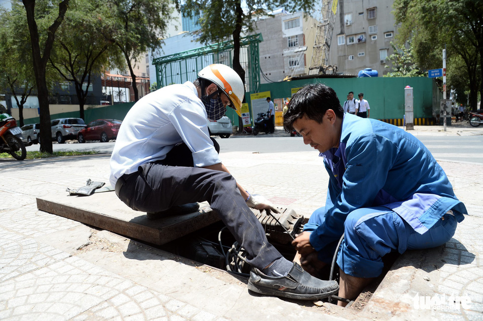 Two men work with underground cables under the scorching sun on Thi Sach Street in District 1, Ho Chi Minh City. Photo: Tu Trung / Tuoi Tre