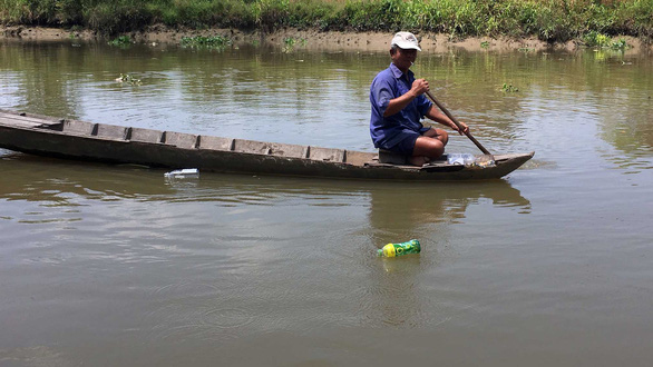 Hai Mum rows his boat on the Co Co River in Tien Giang Province to look for plastic bottles he can sell to scrap dealers to earn money to help others. Photo: My Lang / Tuoi Tre
