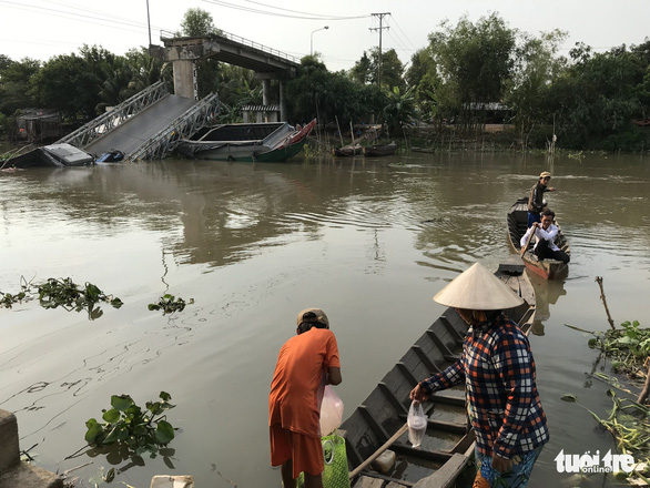 People travels on a boat across the canal as the collapsed bridge is seen in the background. Photo: Ngoc Tai