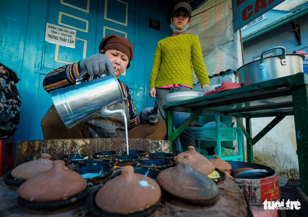 A woman pours powder into a pancake pan to make banh can. Photo: Mai Vinh / Tuoi Tre