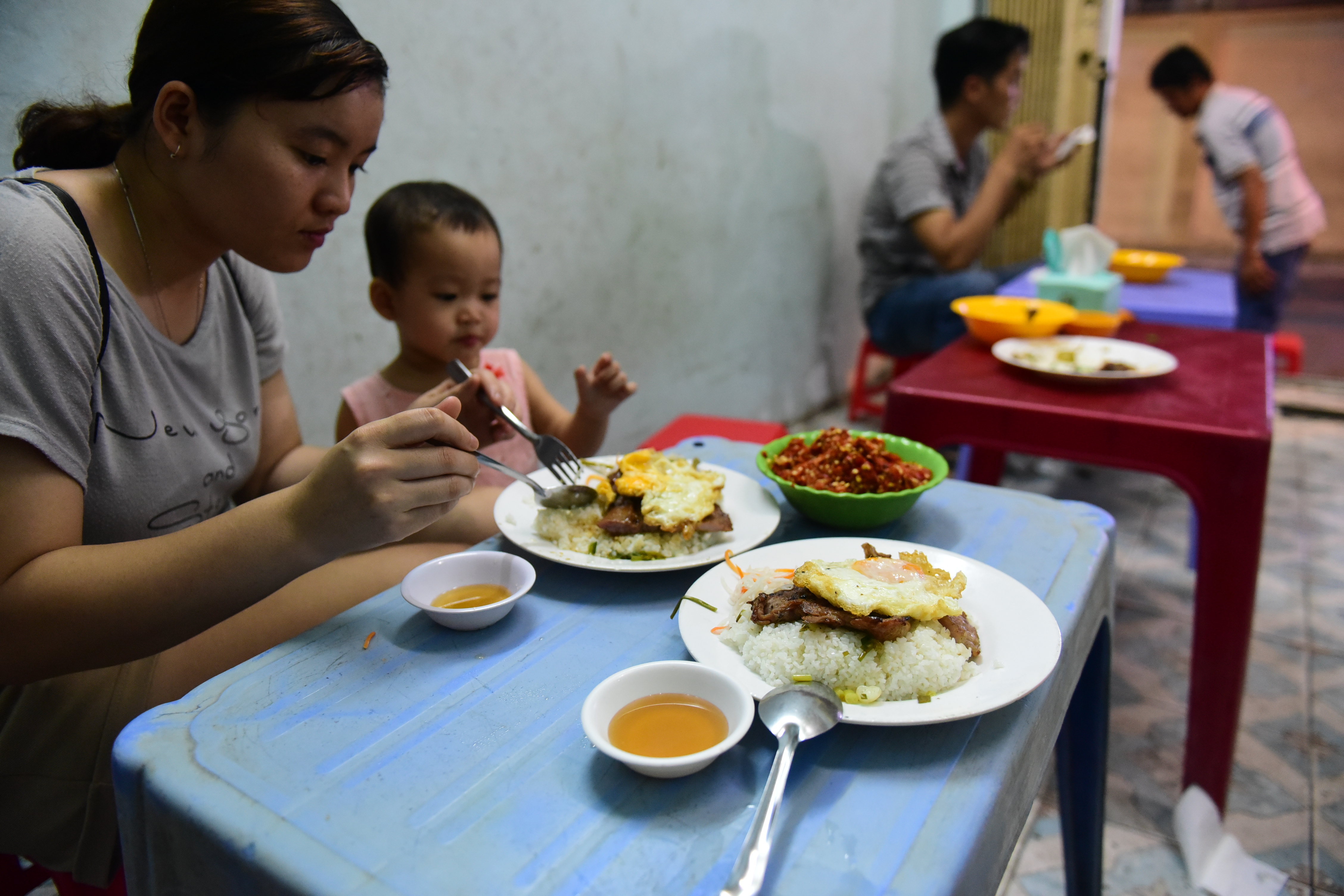 A woman and a kid are having com tam at a stall in an alley on Dinh Tien Hoang Street, Binh Thanh District in the evening. The stall opens until midnight. Photo: Quang Dinh/ Tuoi Tre