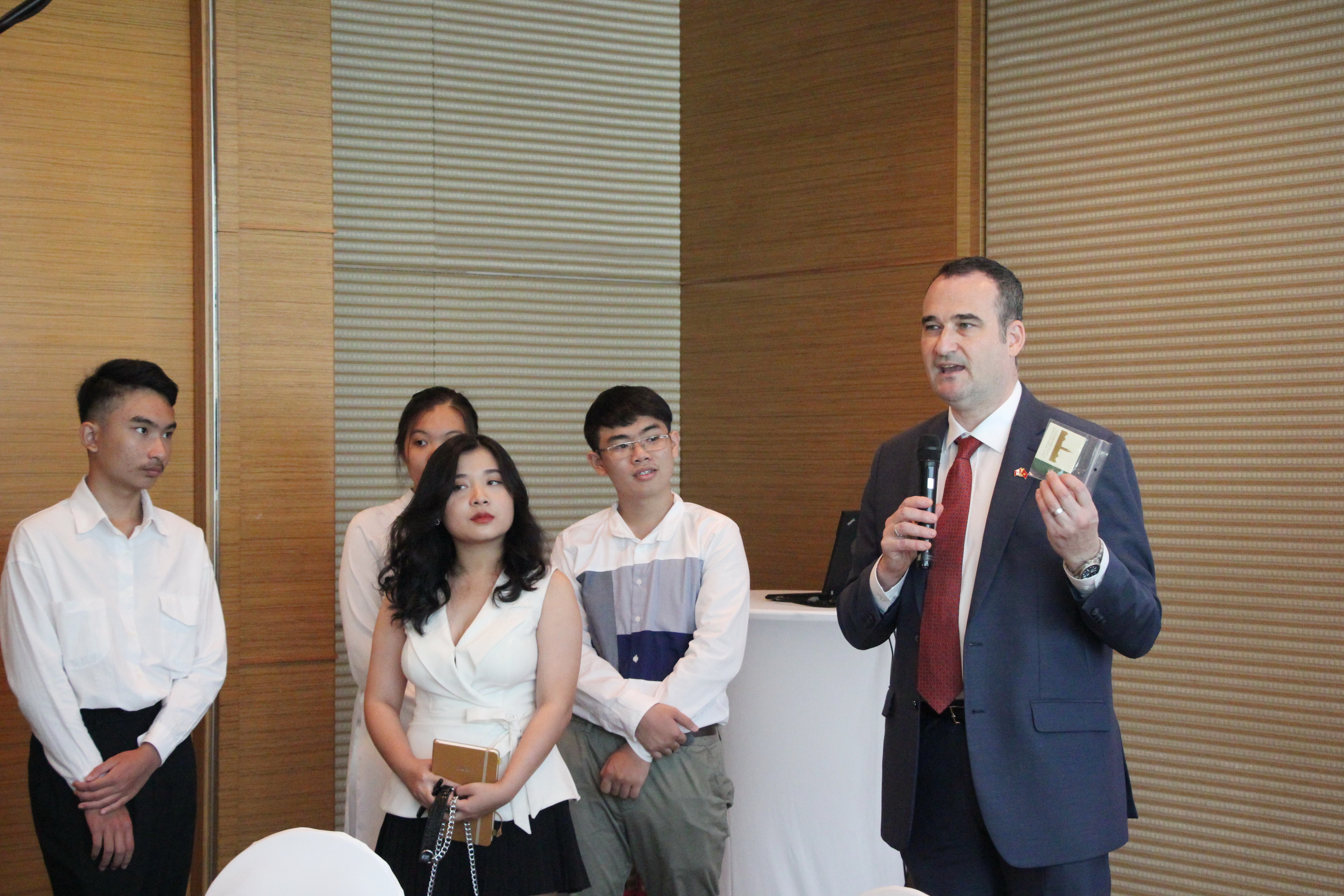 Canadian Consul General Kyle Nunas handles the 'Consul General for a Day' contest's finalists souvenirs made from the original cooper which covered the roofs of Canada's Parliament Buildings from 1918 to 1996 at the at the luncheon on February 19, 2020 in Ho Chi Minh City. Photo: Dong Nguyen/ Tuoi Tre News