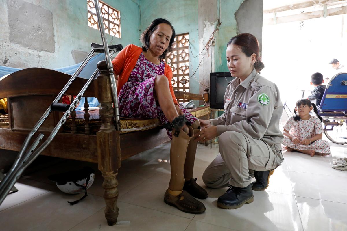 Hoang Thi Hoa, who lost both legs and an arm due to unexploded ordnance (UXO) during the Vietnam War, is assisted by her daughter Nguyen Thi Ha Lan, a member of all-female landmines clearance team, at their house in Quang Tri province, Vietnam March 4, 2020. Picture taken March 4, 2020. Photo: Reuters
