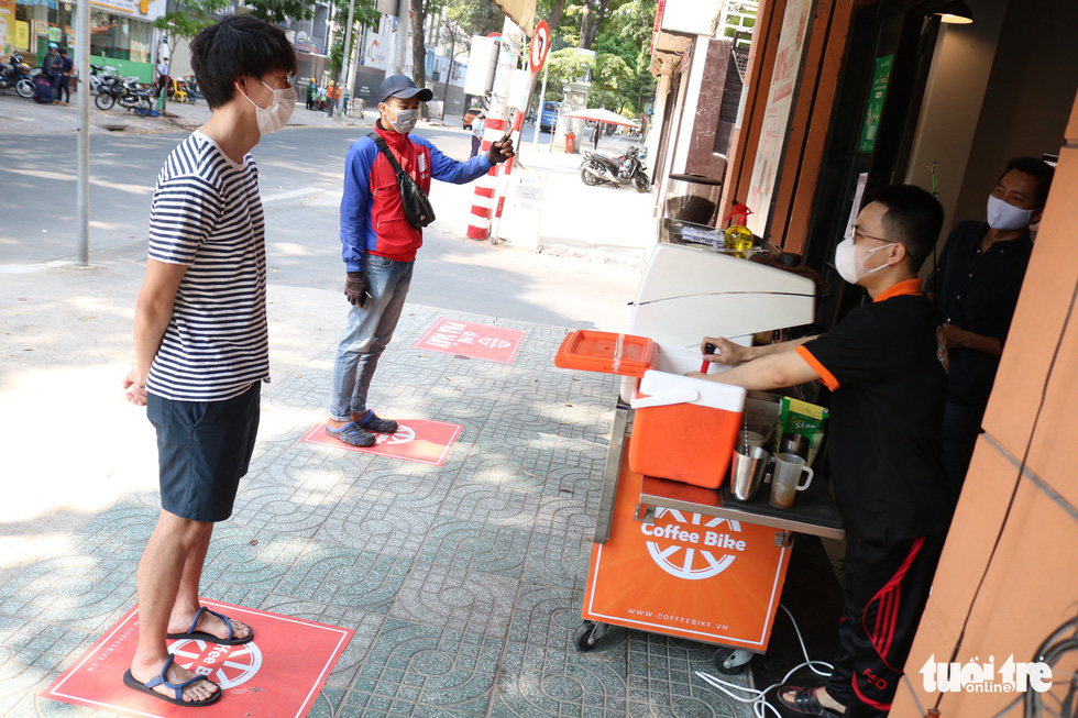Two customers are seen standing distanced from each other on designated spots while waiting to pick up their drinks at a coffee shop in District 1, Ho Chi Minh City, Vietnam, March 29, 2020. Photo: Ngoc Phuong / Tuoi Tre