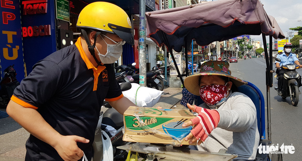 A member of charity group G9 hands a box of instant noodles to a lottery ticket seller on Saigon street. Photo: Duyen Phan/ Tuoi Tre