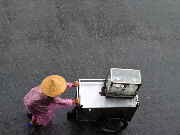 An old woman push street cart in the rain on a street in Binh Thanh District, Ho Chi Minh City. Photo: Ngoc Hien / Tuoi Tre