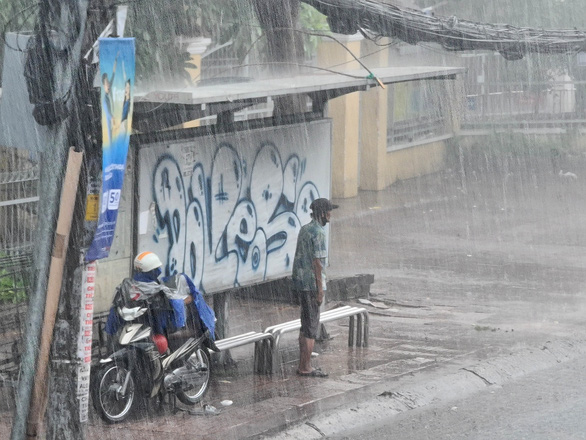 Two people find a shelter from the rain at a bus stop on Le Quang Dinh Street in Binh Thanh District, Ho Chi Minh City. Photo: Ngoc Hien / Tuoi Tre