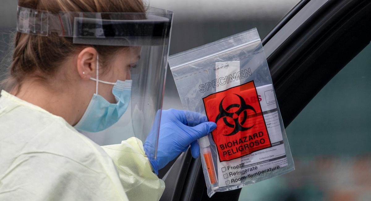 A health worker in protective gear hands out a self-testing kit in a parking lot of Rose Bowl Stadium during the global outbreak of the coronavirus disease (COVID-19), in Pasadena, California, U.S., April 8, 2020. Photo: Reuters