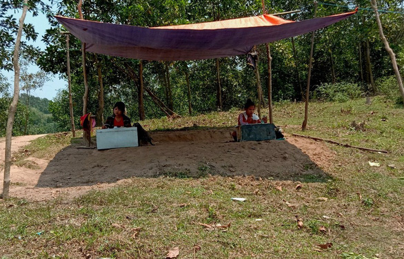 Ho Thi Suong (L) and Ho Thi Tam are seen sitting in a makeshift tent on top of a hill in the north-central province of Quang Tri's Khe Ngai Village for her online classes. Photo: H.S./Tuoi Tre