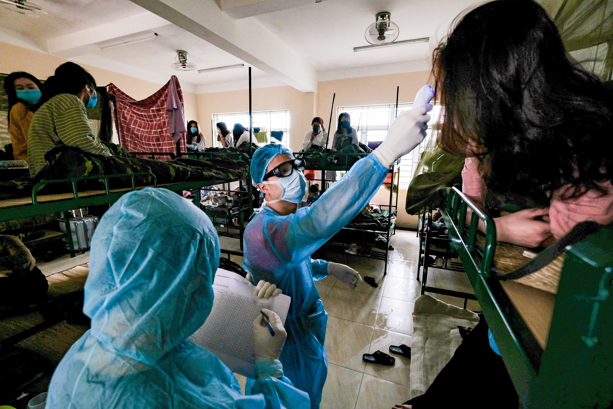 Nguyen Phu Trung goes door to door to measure the body temperature of people isolated at a COVID-19 quarantine facility in Hanoi, Vietnam. Photo: Nam Tran / Tuoi Tre