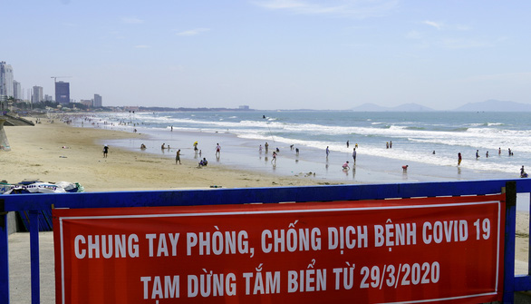 A banner banning beach-going for COVID-19 prevention and control is placed on an embankment of a closed beach in Vung Tau City, Ba Ria – Vung Tau Province, Vietnam, with beachgoers spotted afar, April 26, 2020. Photo: Dong Ha / Tuoi Tre