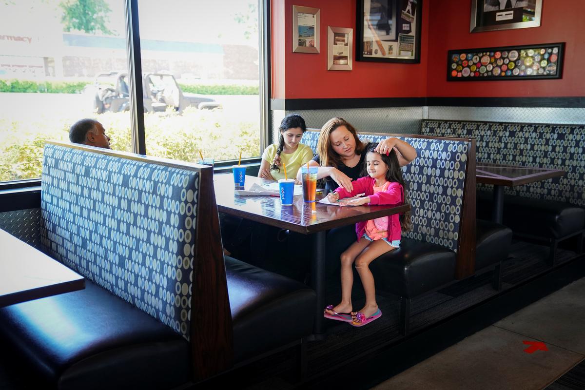 Laura Haque puts a scrunchie in the hair of her daughter Hannah, 5, while eating lunch with her family at Bad Daddy's Burger Bar on the day restaurants and theaters were allowed to reopen to the public as part of the phased reopening of businesses and restaurants from the coronavirus disease (COVID-19) restrictions in Smyrna, Georgia, U.S. April 27, 2020. Photo: Reuters