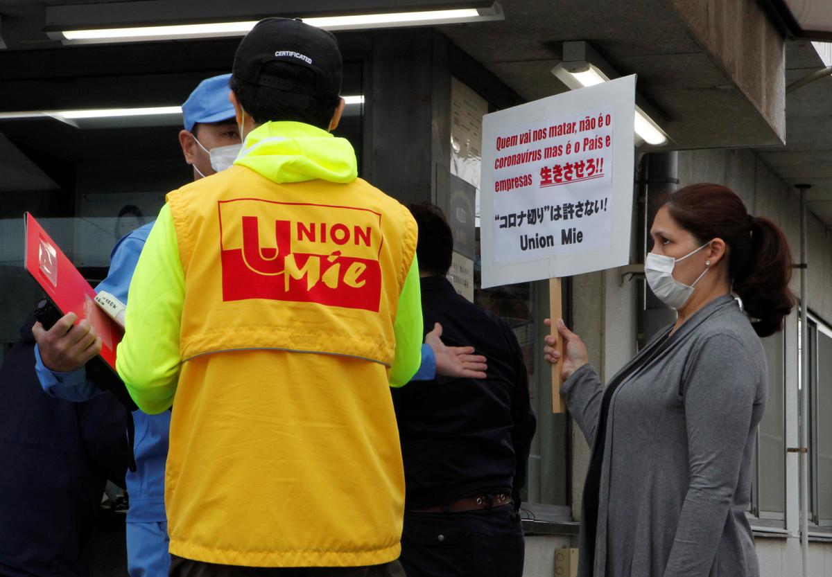 Union organizer Akai Jimbu protests the firing of Japanese-Brazilian Kaori Nakao wearing a protective mask, amid the coronavirus disease (COVID-19) outbreak, in front of the factory she used to work at, while a man tries to stop their protest, in Kiyosu, Aichi Prefecture, Japan April 20, 2020. Photo: Reuters