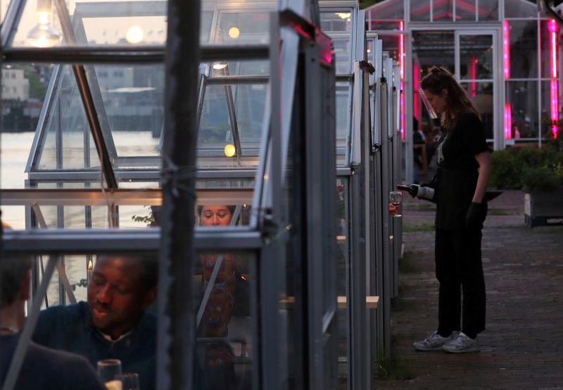 An attendant wearing a clear face shield serve wine to customers through the door of a 'quarantine greenhouse' being tested in which guests can dine at a restaurant in Amsterdam. Photo: Reuters