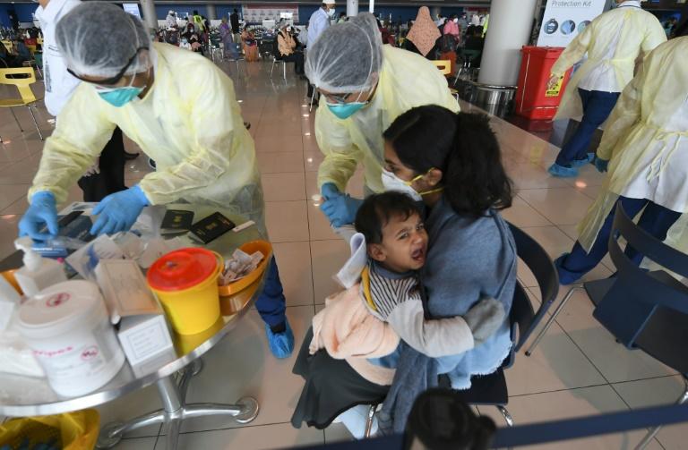 Health workers take a blood test from a child carried by an Indian woman at the Dubai International Airport before they leave the Gulf Emirate on a flight back to their country on May 7, 2020. Photo: AFP
