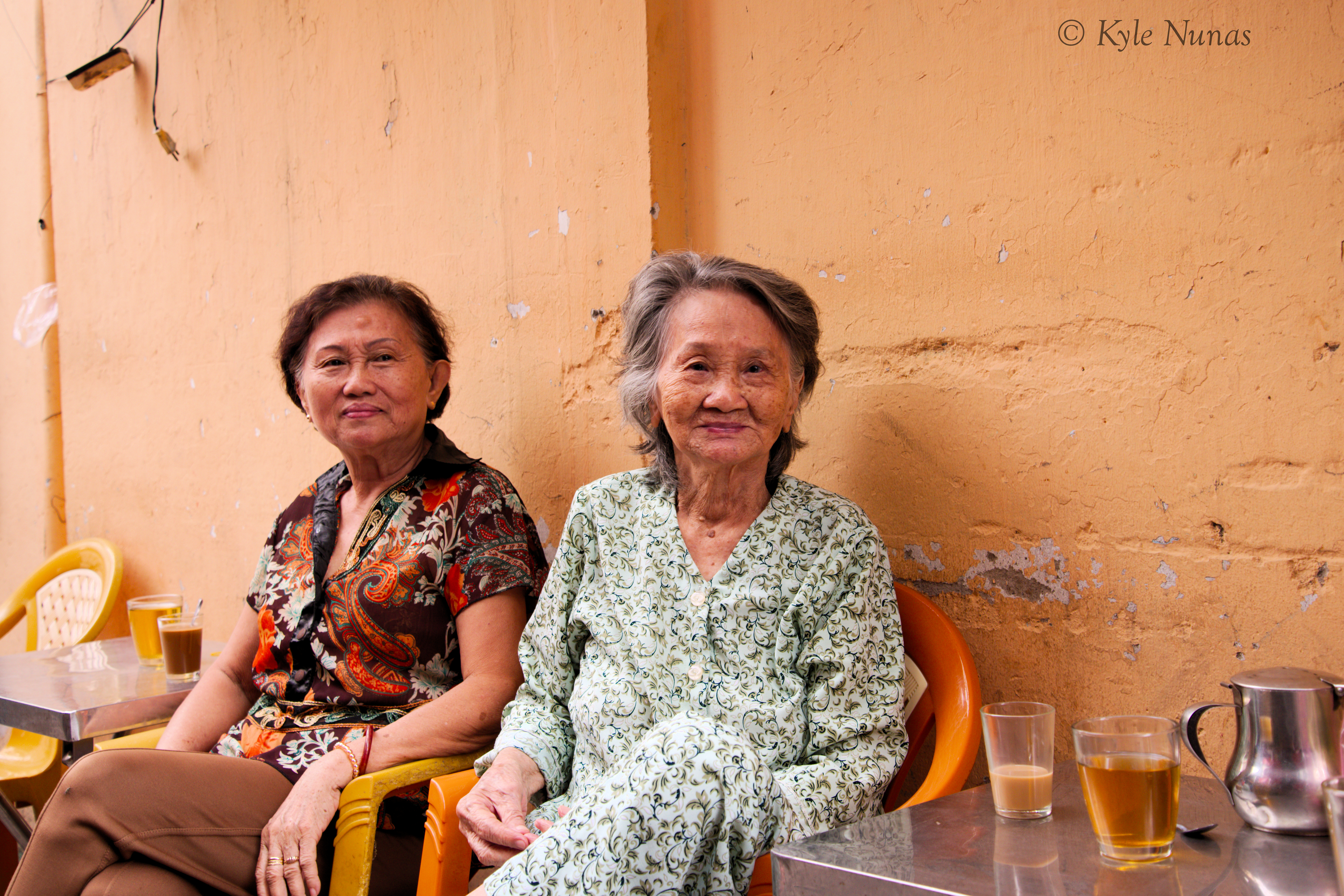 Two women who are having coffee down an alley in Vietnam smile for a photo taken by Kyle Nunas in July 2020.