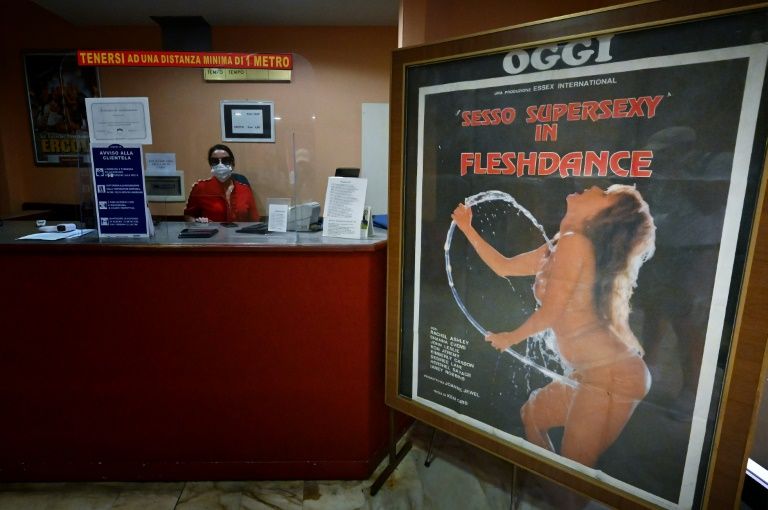 A view taken on August 26, 2020 shows an employee wearing a face mask at the ticket counter and a porn film's poster in the entrance hall of the 'Ambasciatori' (The Ambassadors), Rome's last porn cinema theater. Photo: AFP