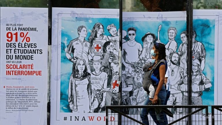A woman with her baby walks past a street art poster created by the French artist Combo for the International Committee of the Red Cross in Paris, August 29, 2020. Photo: AFP