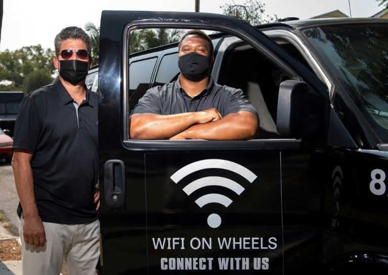Roman Reyna (L) and Kevin Watson (R), of JFK Transportation, pose by one of their minivans that give underserved kids wifi access in Santa Ana, California. Photo: AFP