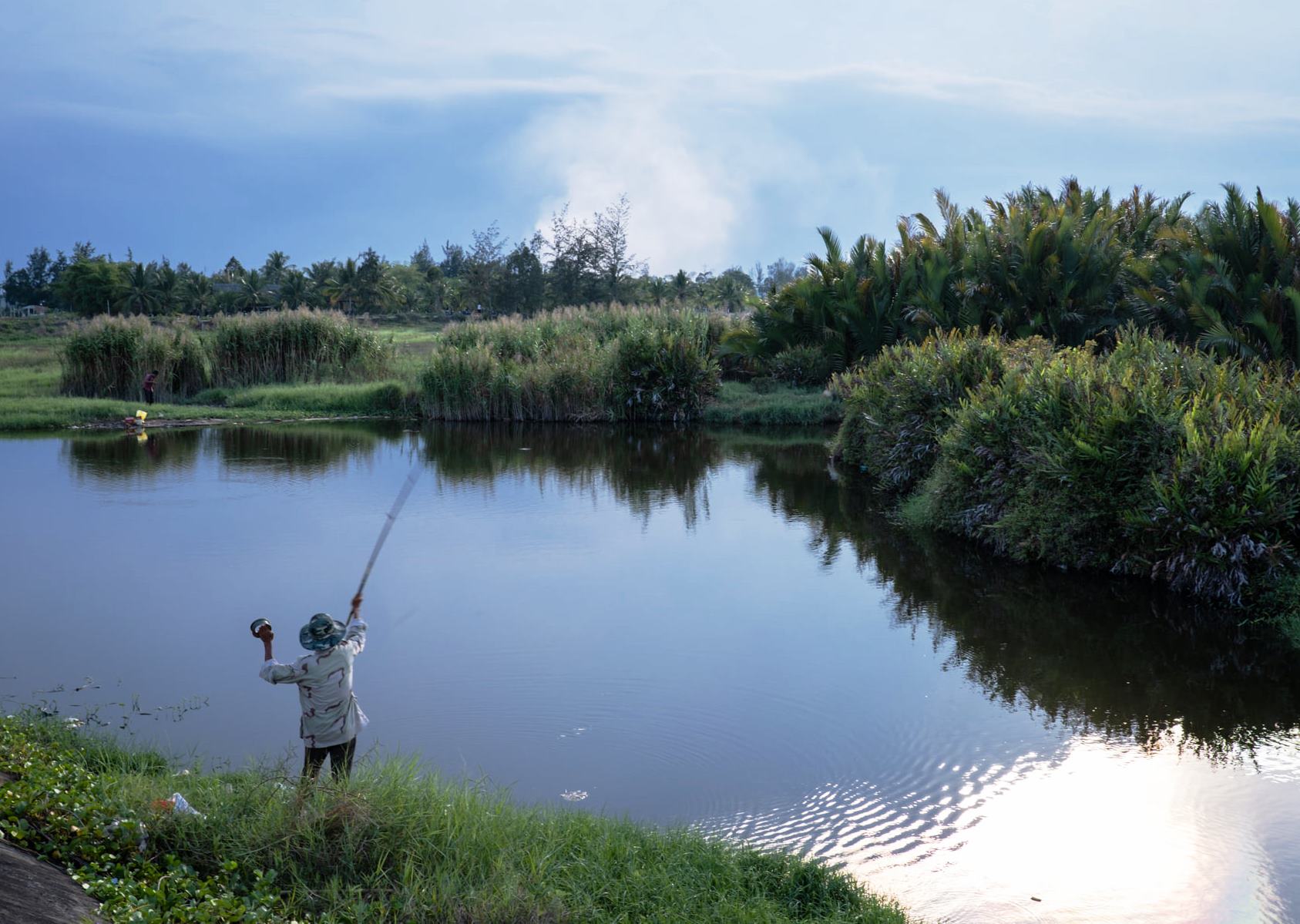 A man fishes at a river with smoke from the Cam Ha landfill in the background in Hoi An City, Quang Nam Province, Vietnam in this photo taken on September 10, 2020. Photo: Etienne Bossot