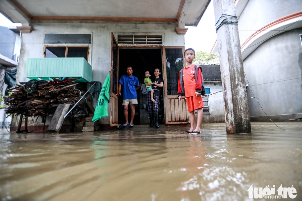 A family stand in front of their house in flooded Quang Phuoc Commune, Quang Dien District, Thua Thien-Hue Province on October 16, 2020. Photo: Nguyen Khanh / Tuoi Tre