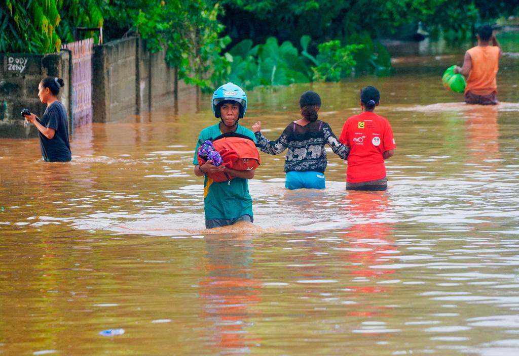 A man wearing a helmet carries his goods through the water in an area affected by floods after heavy rains in Dili, East Timor, April 4, 2021. Photo: Reuters
