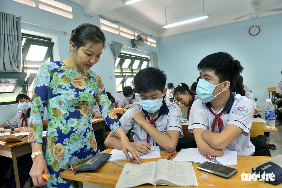 A teacher points to a book opened before two brothers, who sit next to each other in the classroom. Photo: Duyen Phan / Tuoi Tre