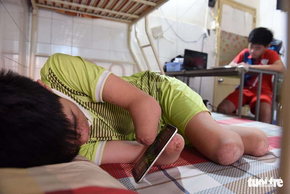 Gia Lam lies on the bed while playing with a cell phone in a 15-square-meter house with his parents and his siblings. Photo: Duyen Phan / Tuoi Tre