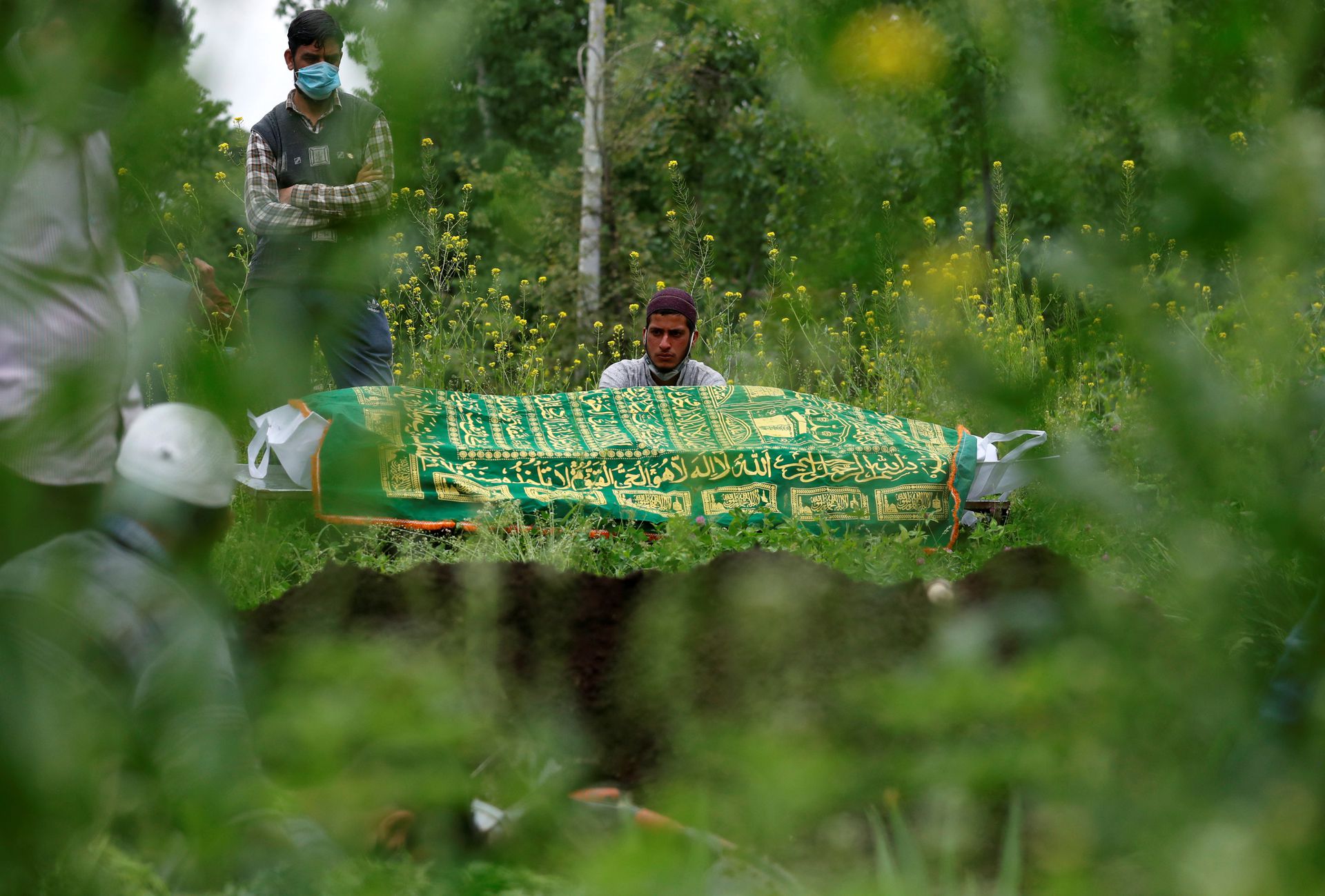 Relatives are seen next to the body of a man who died due to the coronavirus disease (COVID-19), as they wait for a grave to be prepared for his burial at a graveyard on the outskirts of Srinagar May 4, 2021. Photo: Reuters