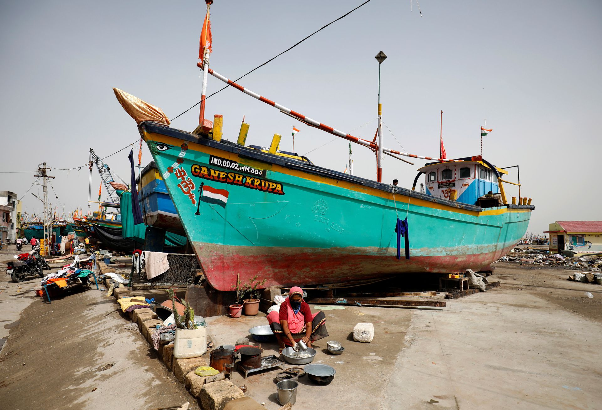A woman prepares food next to docked fishing boats following Cyclone Tauktae in Vanakbara in Diu, India, May 19, 2021. Photo: Reuters