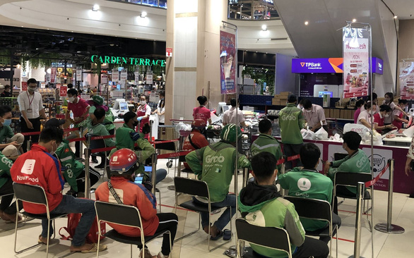 Delivery workers sit in safe distancing while waiting to collect orders for their customers at a supermarket in Ho Chi Minh City. Photo: K.L. / Tuoi Tre