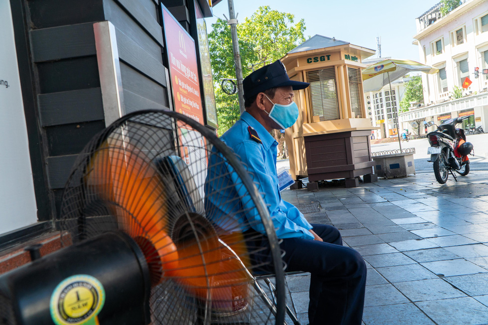 Pham Quang Hop sits next to a working fan during his shift as a security guard in front of a store in Hoan Kiem District, Hanoi, June 20, 2021. Photo: Pham Tuan / Tuoi Tre