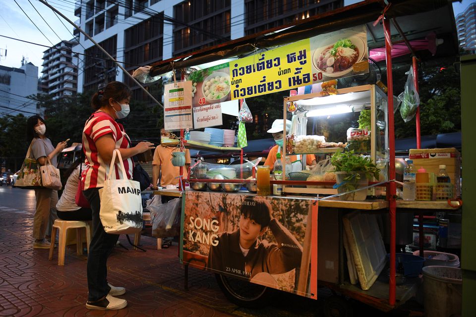 A woman selling street food has her stall decorated with a banner of Korean star Song Kang in Bangkok, Thailand April 29, 2021. Picture taken April 29, 2021. Photo: Reuters