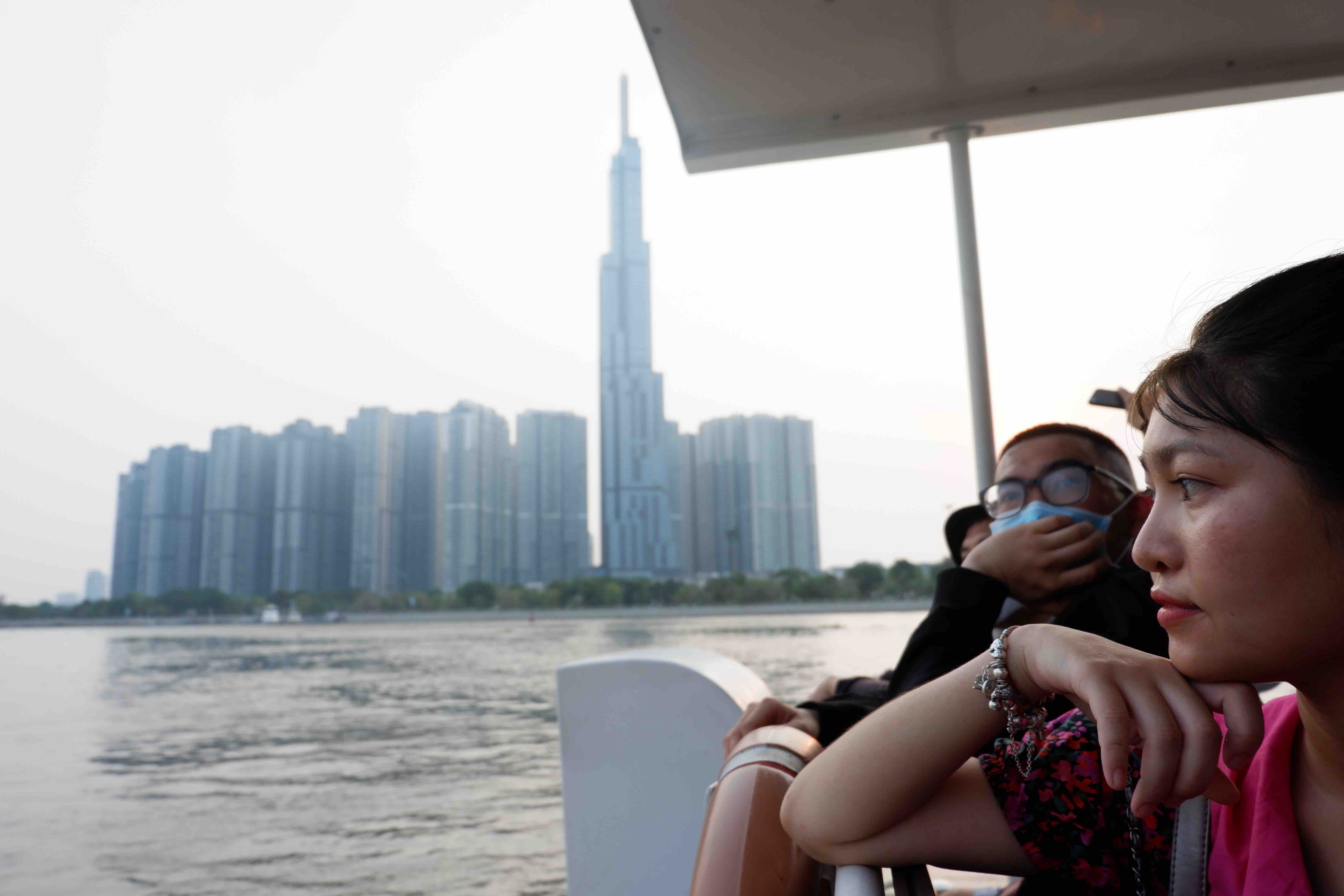 A group of passengers contemplate the sun go down against the blue background of the sky and the iconic Landmark 81 skyscraper in from the Saigon Waterbus. Photo: Linh To / Tuoi Tre
